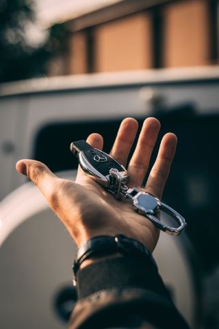 Mano sosteniendo una llave de coche Mercedes frente a un vehículo