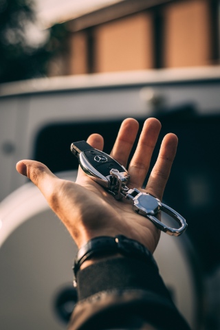 M&atilde;o a segurar uma chave de carro Mercedes em frente a um ve&iacute;culo