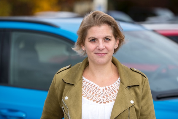 Frau in olivfarbener Jacke steht vor einem blauen Auto