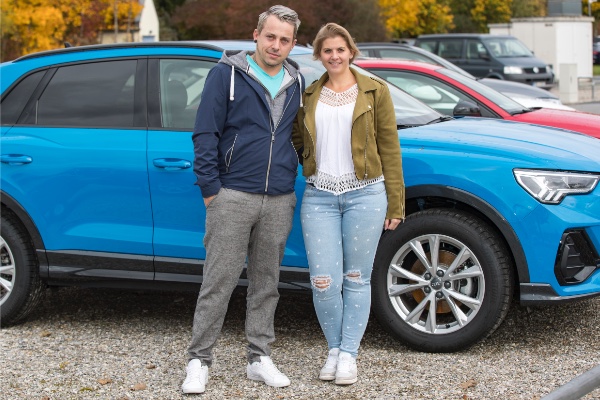 Paar steht vor einem blauen Audi-SUV auf einem Parkplatz