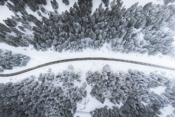 Luftaufnahme einer Stra&szlig;e, die sich durch einen verschneiten Wald schl&auml;ngelt