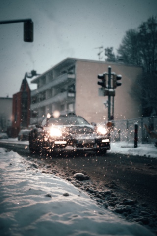 Auto f&auml;hrt bei Schneefall mit eingeschaltetem Licht durch eine winterliche Stra&szlig;e