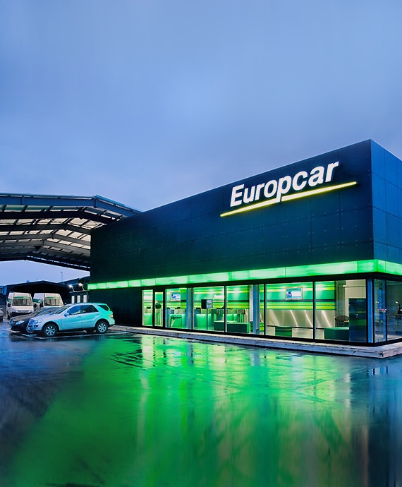 Agence Europcar &eacute;clair&eacute;e en vert au cr&eacute;puscule avec des voitures de location devant