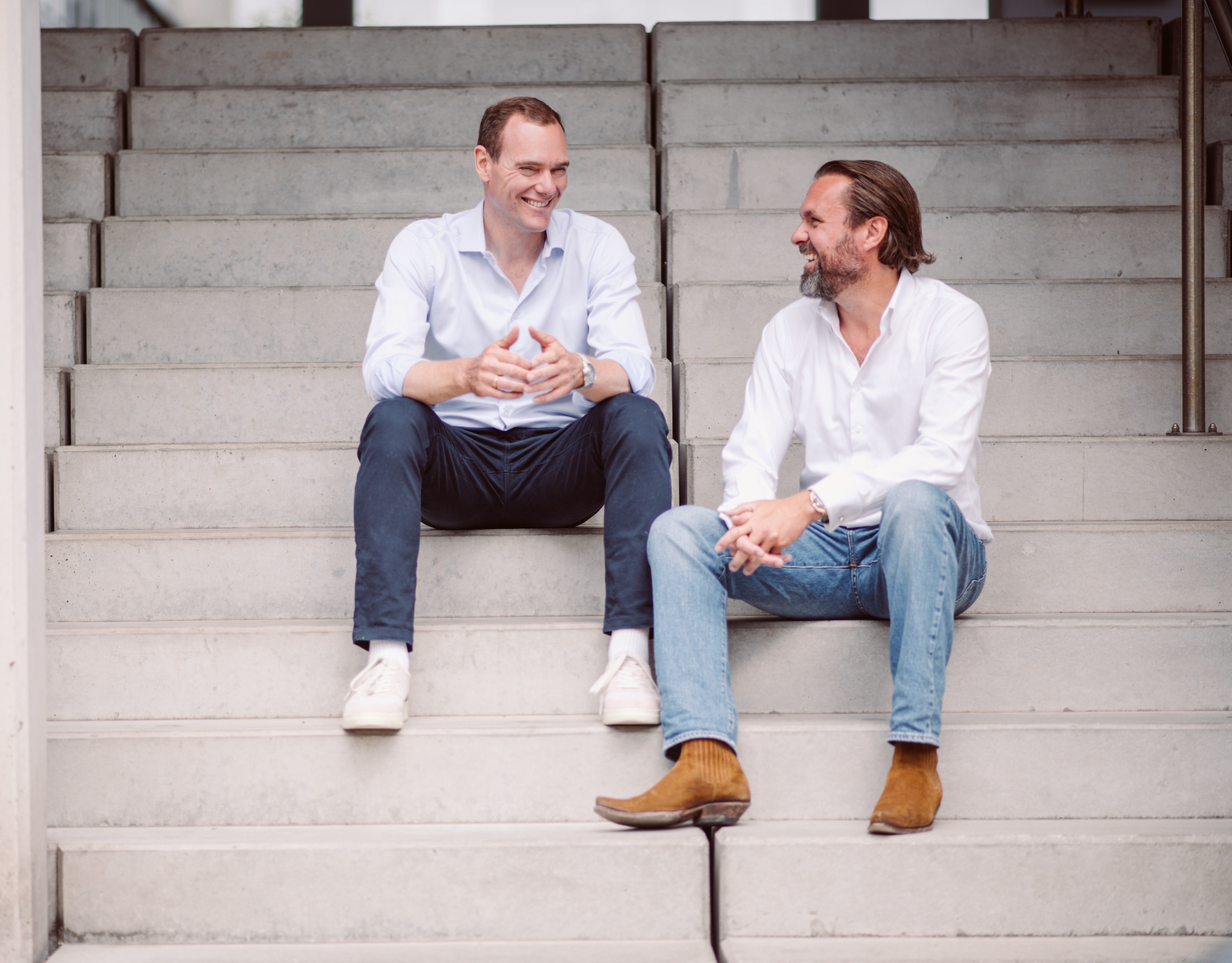 Two laughing ONLOGIST managing directors sitting on concrete steps